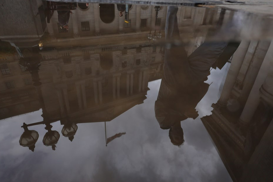 A person walks past the Bank of England, reflected in a puddle, in London, Britain, September 23, 2024.