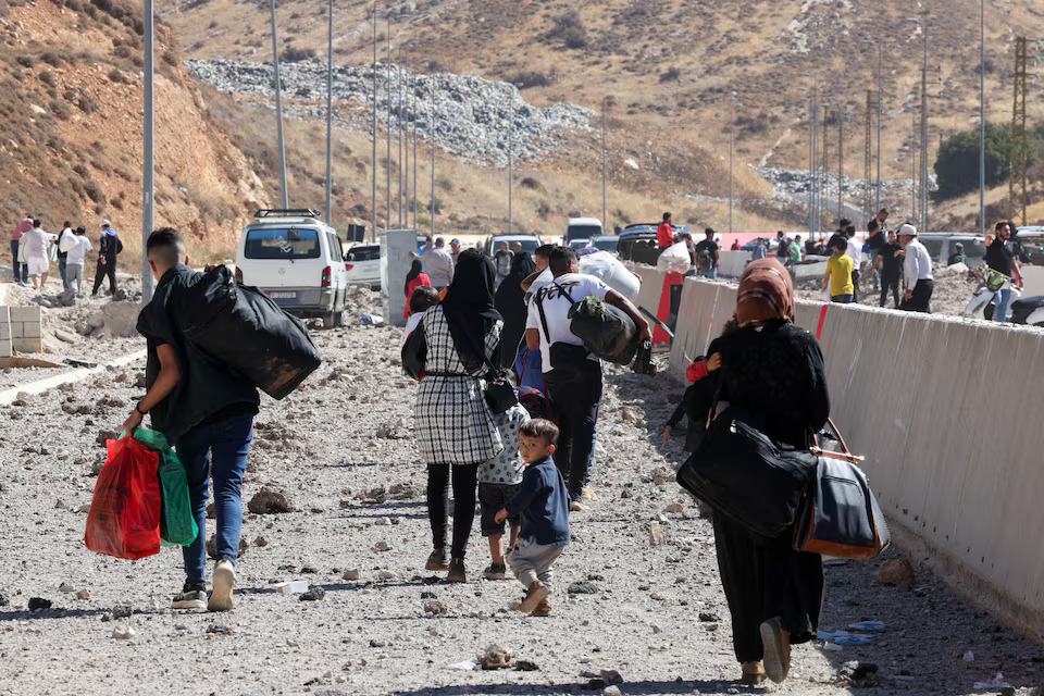 People carry their belongings while walking on the rubble, after an Israeli strike, as they flee Lebanon due to ongoing hostilities between Hezbollah and Israeli forces, at Masnaa border crossing with Syria, in Lebanon on October 4 — Reuters photo