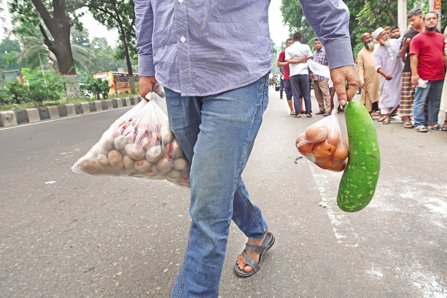 A man carries home potatoes, eggs, and a bottle gourd he bought from an Open Market Sale (OMS) point at Abdul Goni Road in the city on Tuesday, while others wait in line (in the background) to purchase agricultural produce at subsidised rates. The government started selling 10 agricultural items at affordable prices under the OMS programme