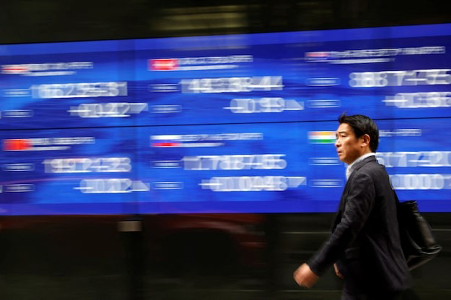 A passerby walks past an electric monitor displaying various countries' stock price index outside a bank in Tokyo, Japan, March 22, 2023.