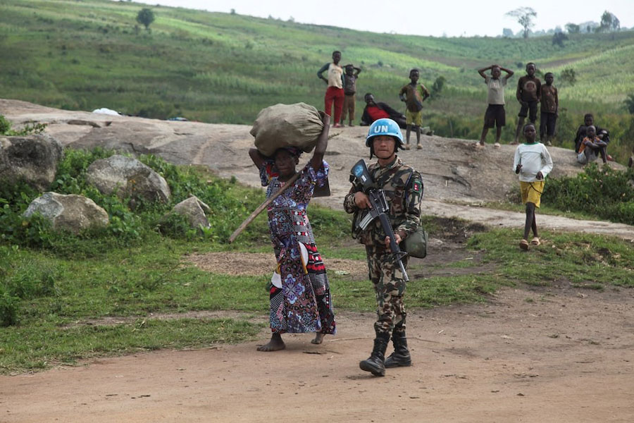 A Nepalese peacekeeper from the United Nations Organization Stabilization Mission in the Democratic Republic of the Congo (MONUSCO) escorts an internally displaced Congolese woman returning from the fields carrying a bag of her harvest on her head, as part of the secure harvest operation within Fataki, in Ituri province, near North Kivu province of the Democratic Republic of Congo December 12, 2024.