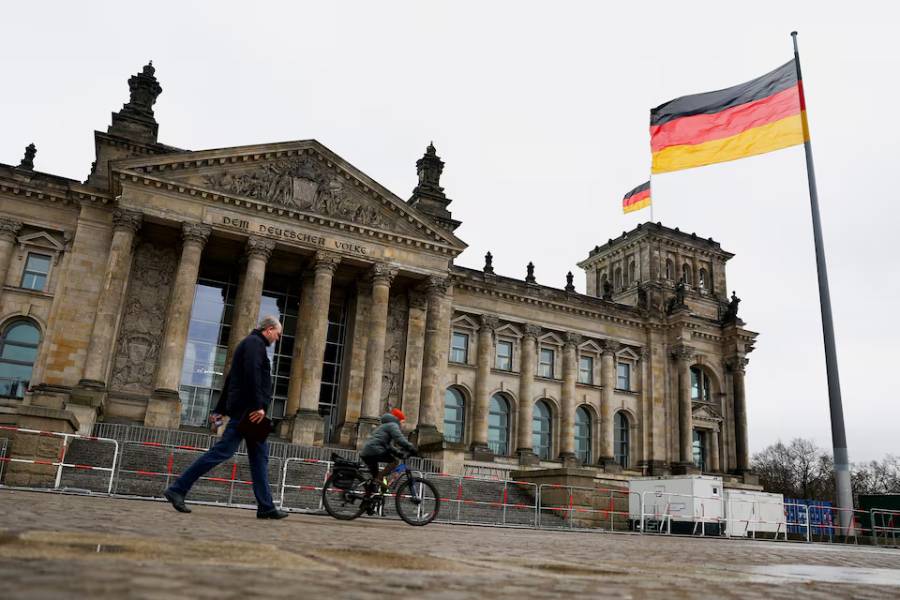 A cyclist and a pedestrian pass by the Reichstag building as the German national flag flutters, on the day of a confidence vote called by German Chancellor Olaf Scholz to pave way for snap election, in Berlin, Germany, December 16, 2024.
