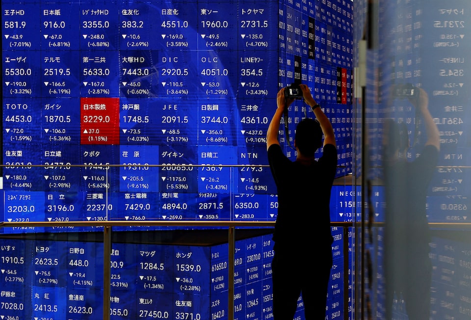 A man takes a photo next to an electronic stock quotation board inside a building in Tokyo, Japan August 2, 2024. REUTERS/Issei Kato/File Photo
