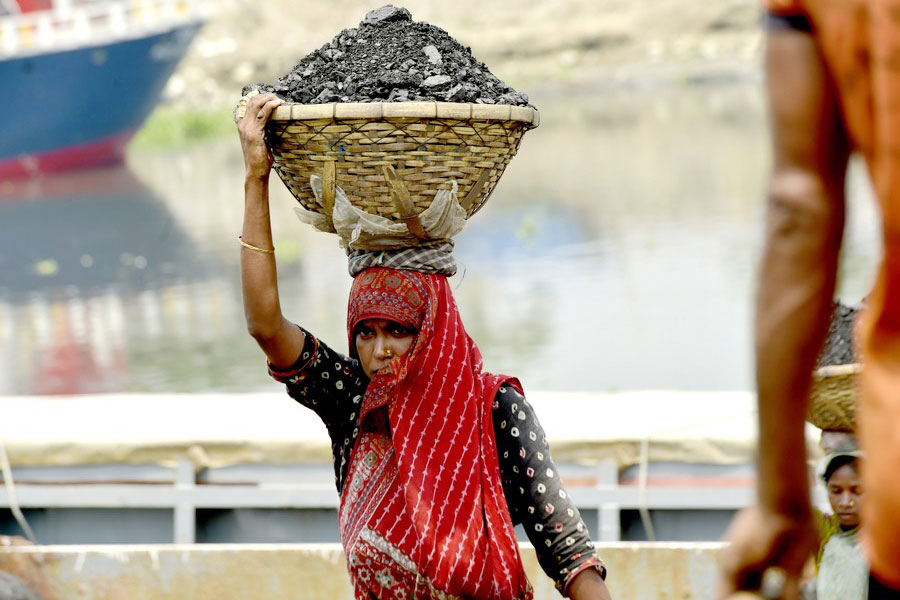 A female labourer carries a basket filled with coal at a river bank in Dhaka, Bangladesh on April 30, 2023