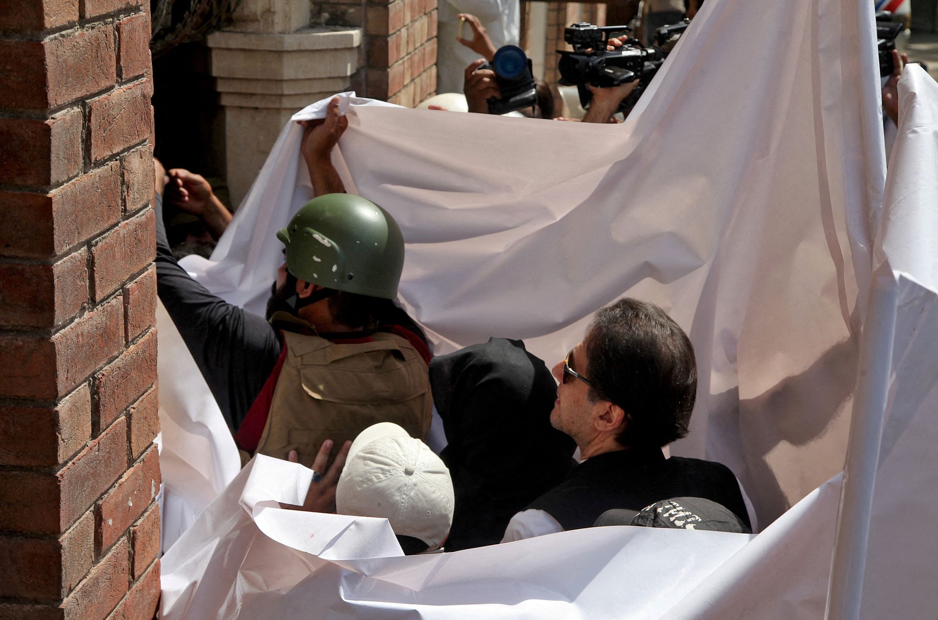 Pakistan's former Prime Minister Imran Khan and his wife Bushra Bibi are covered with a white sheet as they arrive to appear at the High Court in Lahore, Pakistan, May 15, 2023. REUTERS/Mohsin Raza