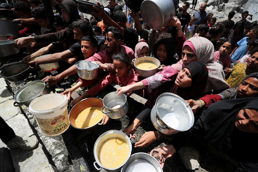 Palestinians wait to receive food cooked by a charity kitchen, in Jabalia, in the northern Gaza Strip, May 19, 2025.