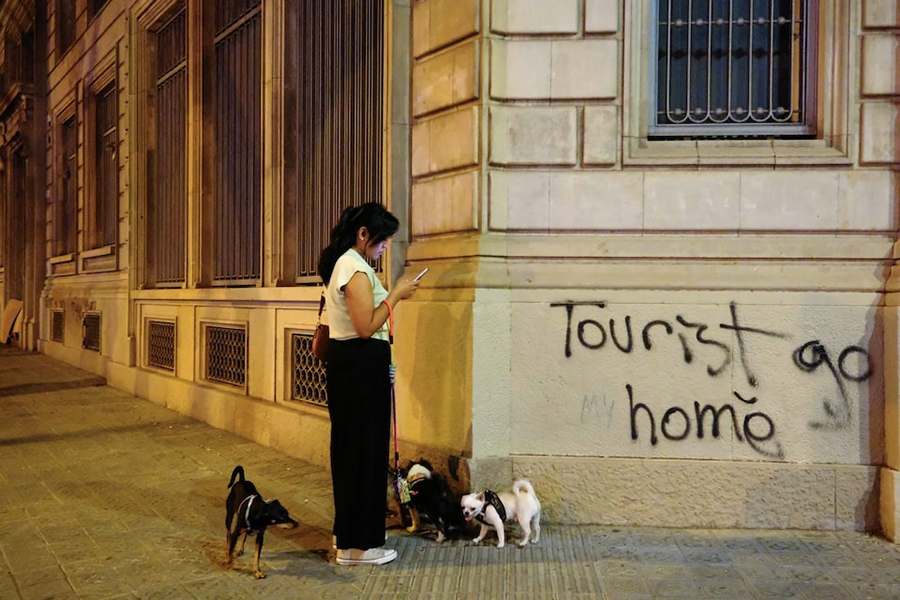 A woman walks with her dogs as she reads a message on her phone next to a graffiti on a wall in Barcelona, Spain on August 29, 2024 — Reuters/File