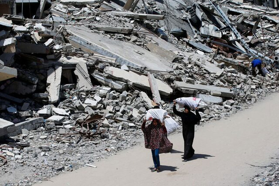 A Palestinian woman and a girl carrying bags of firewood walk by the rubble of houses, in Gaza City, May 20, 2025.
