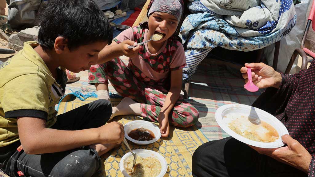 Palestinian woman, Basma Al-Sheikh Khalil, eats with her grandchildren in front of the tent they took shelter after being displaced, in Deir Al-Balah, in the central Gaza Strip, May 21, 2025. REUTERS