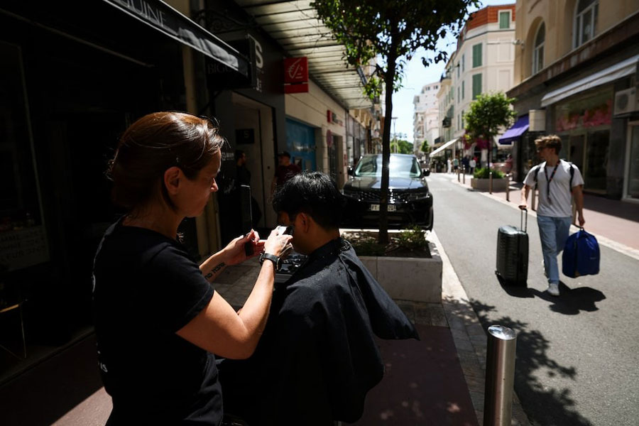 A hairdresser works on a client's haircut in the street due to not enough light in her hair salon, following a major electricity outage, during the 78th Cannes Film Festival in Cannes, France May 24, 2025.