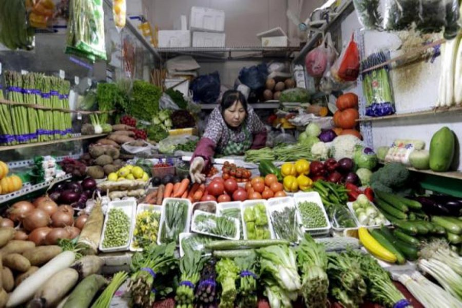 A vendor reaches out for vegetables at her shop in a market in Beijing. — Reuters