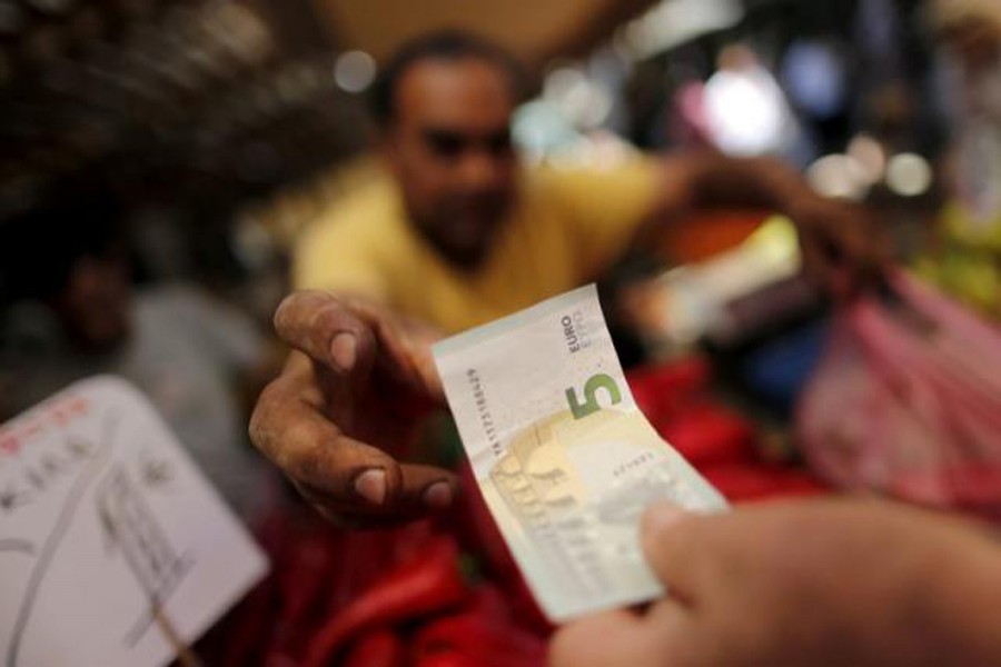 A vendor receiving a five-Euro bank note from a customer at the central market in Athens, Greece — Reuters