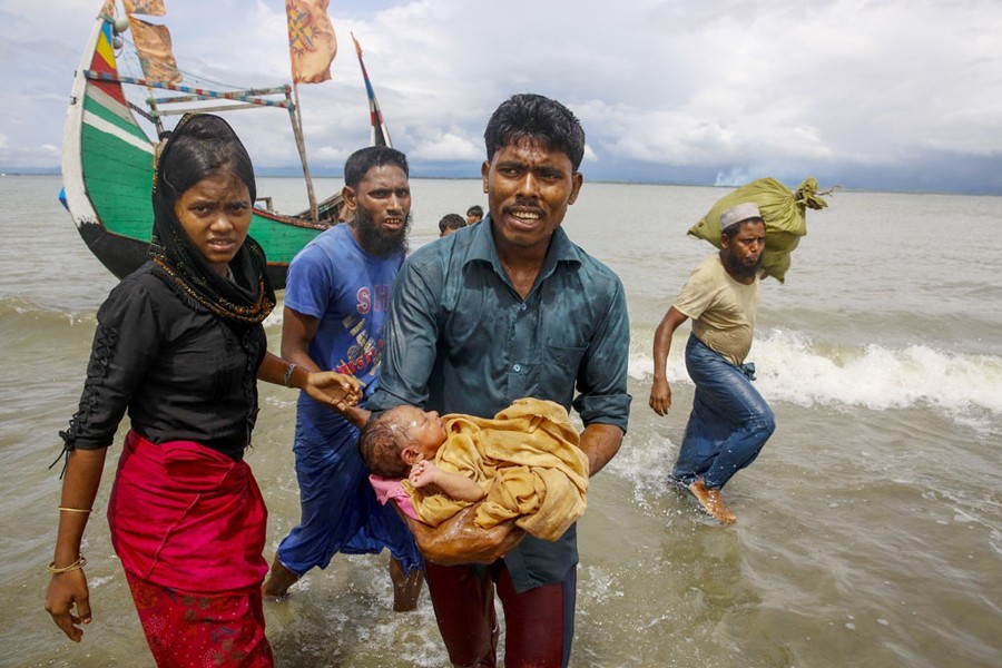 A file photo showing a Rohingya man carrying an infant to the shore from a boat that arrived at Shah Porir Dwip in Bangladesh from Rasidong in Myanmar recently. A US government investigation has found that Myanmar's military waged a planned, coordinated campaign of mass killings, gang rapes and other atrocities against the Southeast Asian nation's Rohingya Muslim minority — Reuters