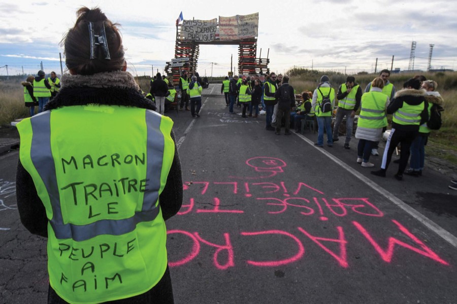MACRON IS A BELLWETHER, BECAUSE WHAT HAPPENS IN FRANCE WILL NOT STAY IN FRANCE: A Yellow vests (Gilets jaunes) protester with the words written on the back of her vest that read, 'Macron (referring to the French President) traitor, the people are hungry' blocks the road leading to the Frontignan oil depot in the south of France, as they demonstrate against the rise in fuel prices and the cost of living on December 03, 2018. —Photo: AFP