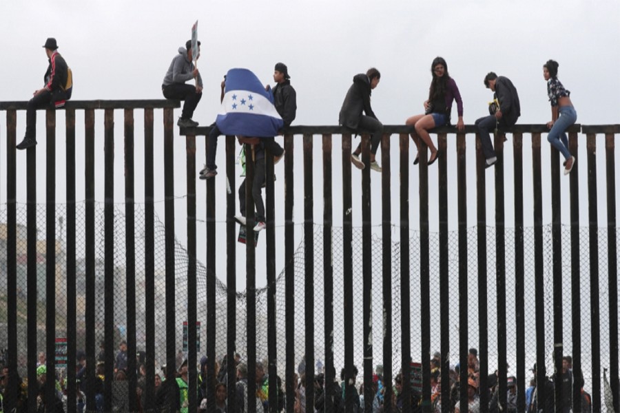 Members of a migrant caravan from Central America and their supporters sit on the top of the US-Mexico border wall at Border Field State Park before making an asylum request in San Diego, California on April 29, 2018. —Photo: Reuters