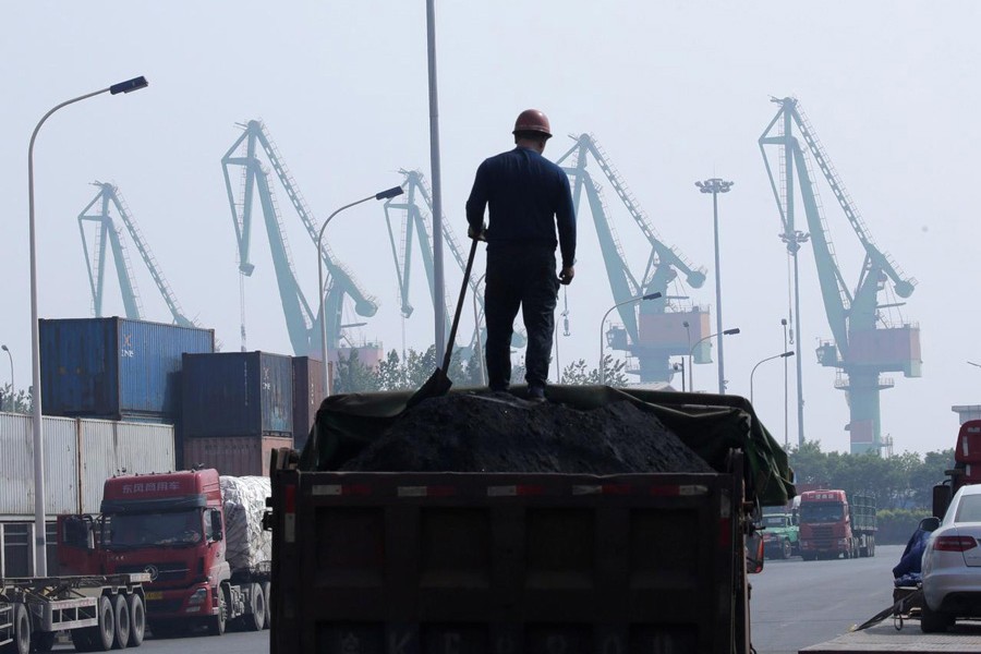 A labourer loading coal in a truck next to containers outside a logistics centre near Tianjin Port, in northern China — Reuters