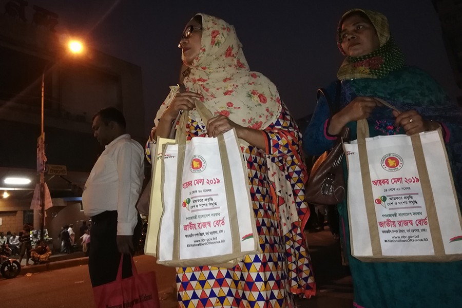 Two women wait for transport at Farmgate in the city on Monday to return to their home after submitting tax returns at the ongoing Income Tax Fair-2019 — FE photo