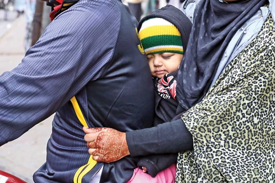 A baby finds a cosy place between its father and mother during a motorcycle ride on Thursday as the city is shivering in the cold with temperature plummeting to 16 degrees Celsius — FE photo by Shafiqul Alam