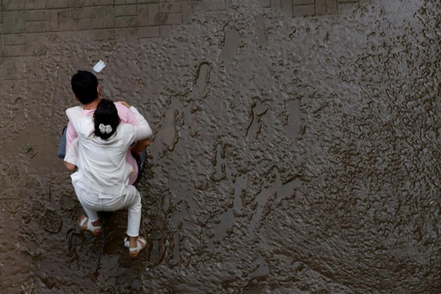A man crosses a mud-covered trail carrying his wife on his back at a flooded Han River park in Seoul, South Korea, August 04, 2020. REUTERS