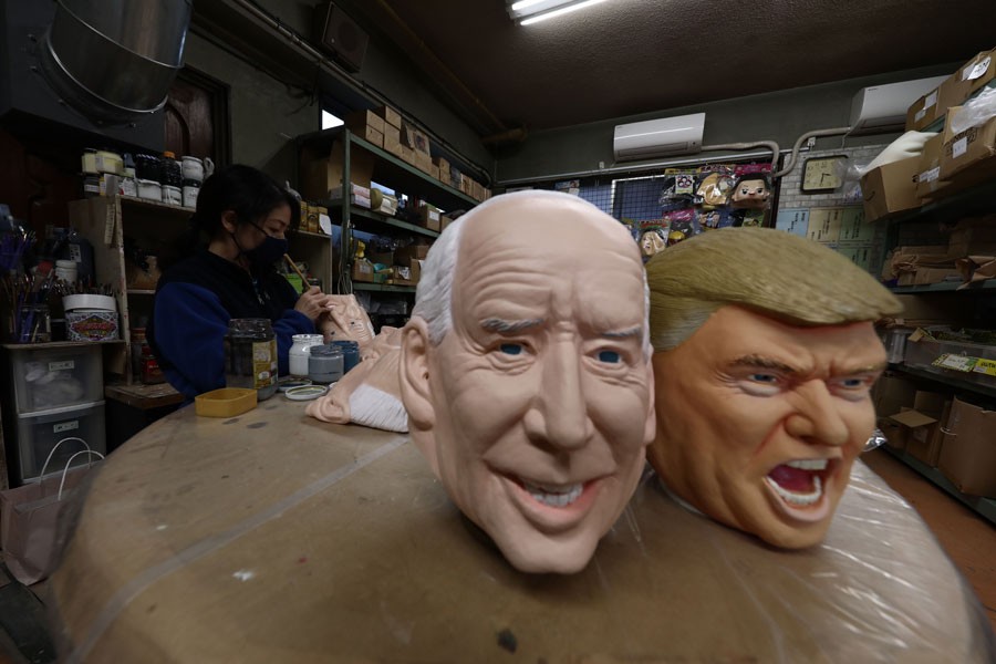 An employee works next to masks of US President-elect Joe Biden (L) and US President Donald Trump at the Ogawa Studios mask factory in Saitama, north of Tokyo on November 12, 2020. —AFP